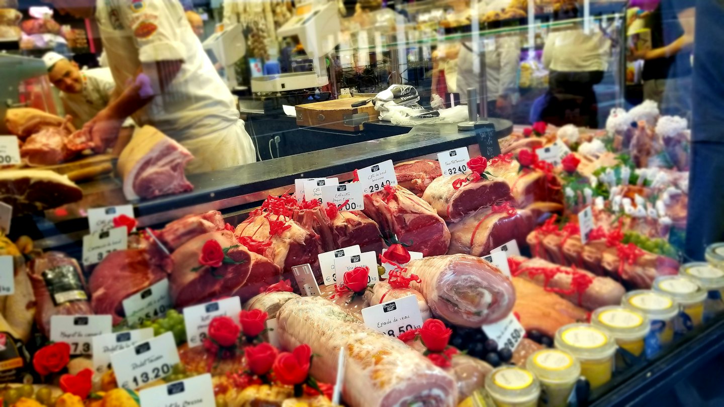 A butcher prepares fresh meat behind a full deli display case.